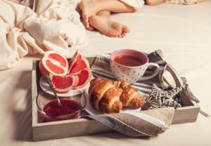 Breakfast with croissant on service tray on the bed near sleeping person