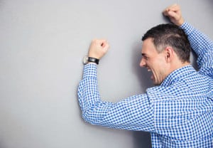 Angry man shouting and hitting gray wall