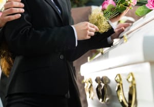 Mourning man and woman on funeral with pink rose standing at casket or coffin